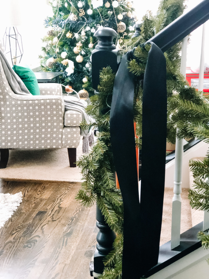 how to hang garland on a staircase - black satin ribbon and pre-lit garland on staircase banister for Christmas - This is our Bliss